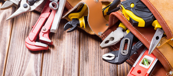 A leather tool belt on a wooden surface holds various tools, including pliers, wrenches, and a tape measure, conveying readiness and craftsmanship.
